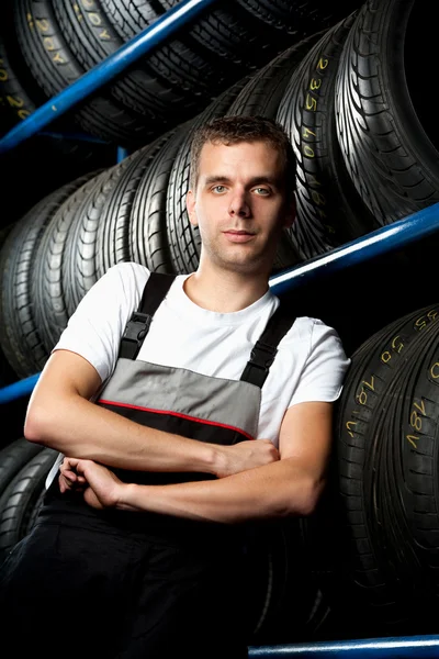 Jovem mecânico em pé ao lado de prateleiras de pneus — Fotografia de Stock