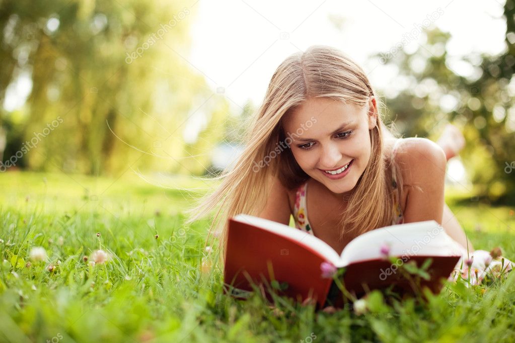 Young woman reading book at park lying down on grass