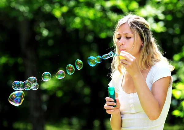 Junge Frau pustet Blasen im Freien Stockbild