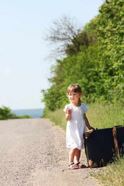 Красивая маленькая девочка на дороге с чемоданом — стоковое фото