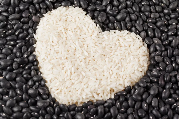 Grãos de arroz em forma de coração isolados nos grãos escuros — Fotografia de Stock