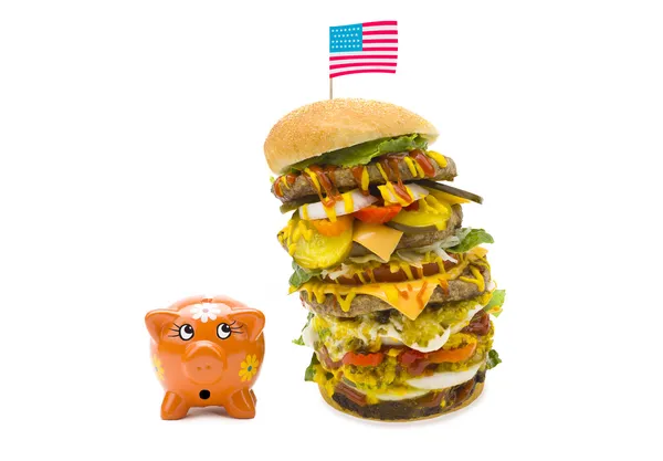 Enormous burger falling over on piggy bank — Stock Photo, Image