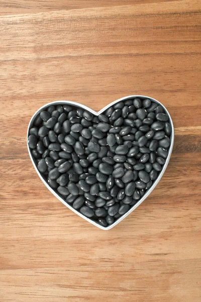 Fagioli neri su un contenitore a forma di cuore — Foto Stock