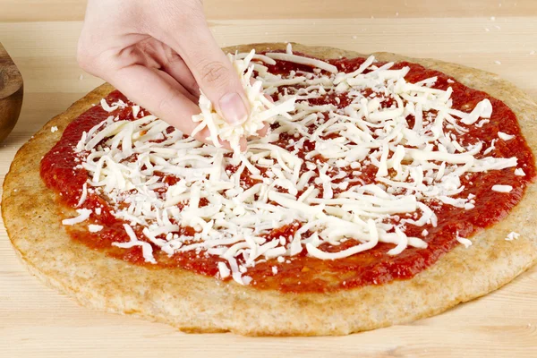 Mão estendendo queijo em uma massa de farinha de pizza — Fotografia de Stock