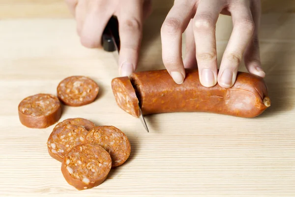 Human hand cutting a sausage — Stock Photo, Image