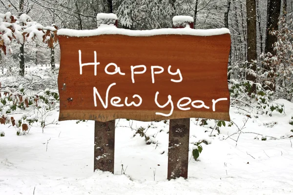 С Новым годом, написанным на деревянной вывеске в снежных лесах зимой — стоковое фото