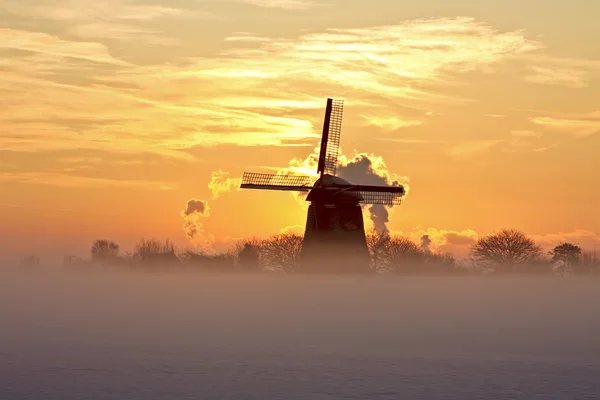 Traditionelle Windmühle in Schnee und Nebel auf dem Land aus den Niederlanden bei Sonnenuntergang — Stockfoto