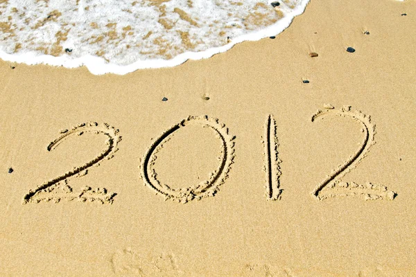 La bienvenida del nuevo año 2012, mensaje en la arena en la playa cerca del océano — Foto de Stock