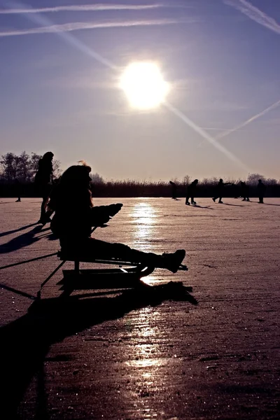 Sledging y patinaje sobre hielo en un frío día de invierno con puesta de sol púrpura en el campo de los Países Bajos —  Fotos de Stock