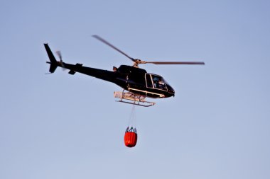 Fire fighting helicopter with waterbag on his way to combat the forest fire clipart