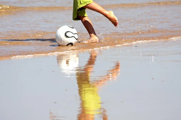 Молодой человек играет в футбол на берегу моря — стоковое фото