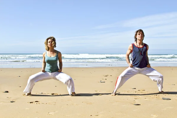 Pareja joven haciendo ejercicios de yoga en la playa — Foto de Stock