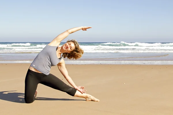Žena dělá jóga cvičení na pláži — Stock fotografie
