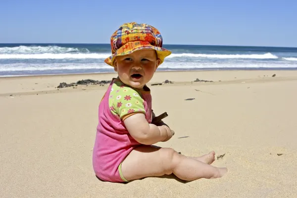 Schattig klein babymeisje zitten in het zand op het strand — Stockfoto