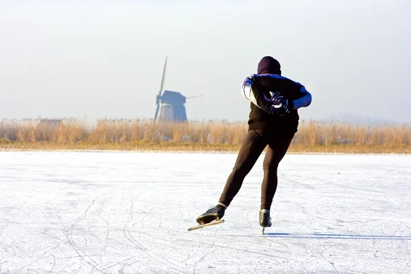 Généralement hollandais : patinage sur glace sur un lac gelé avec vue sur un moulin à vent lors d'une froide journée d'hiver — Photo