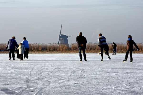 Typically dutch: ice skating on a frozen lake with view on a windmill on a cold winterday — Stock Photo, Image