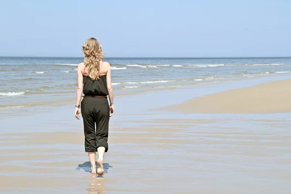 Schöne junge blonde Frau, die am Strand entlang geht — Stockfoto
