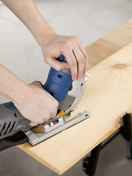 Mão usando serra elétrica para cortar folha de madeira — Fotografia de Stock