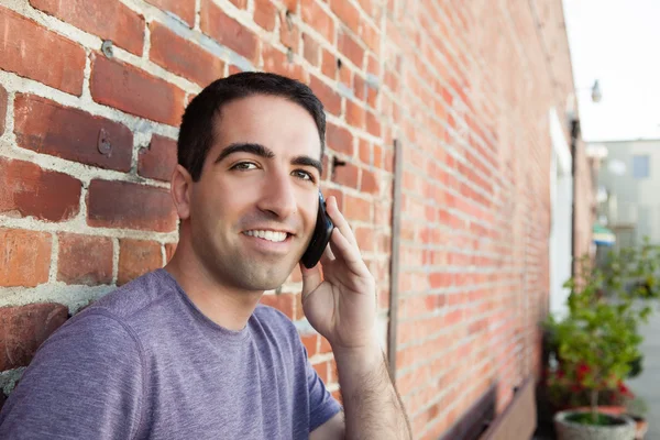 Ładny facet na telefon przez mur z cegły — Zdjęcie stockowe