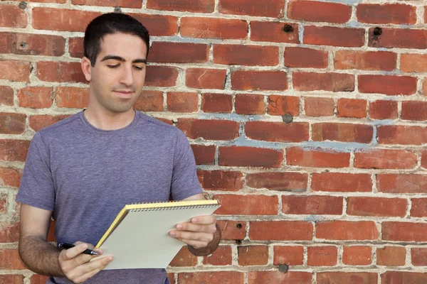 Cute guy using paper pad by brick wall — Stock Photo, Image