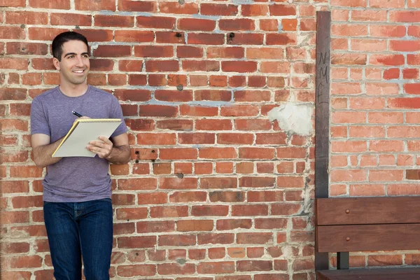 Ładny człowiek pisze na pad papieru przez mur z cegły — Zdjęcie stockowe