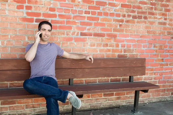 Парень, сидящий на скамейке и разговаривающий по телефону — стоковое фото