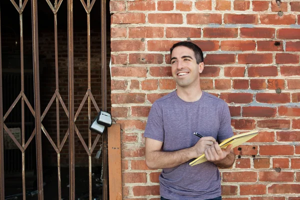 Guy souriant avec du papier contre un mur de briques — Photo
