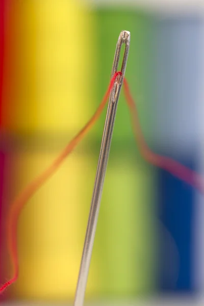 Renkli arka plan üzerinde kırmızı iplik ile iğne — Stok fotoğraf