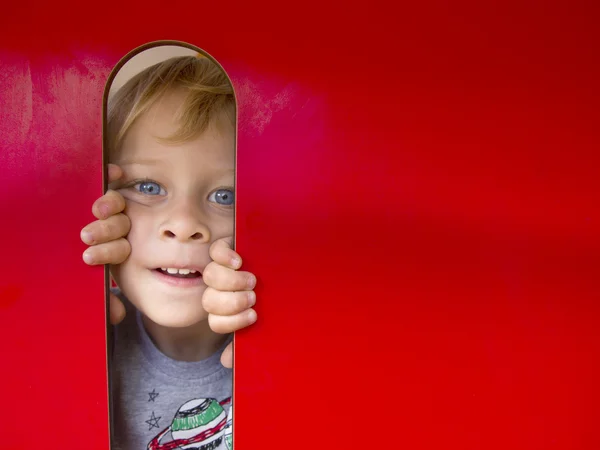 Młody chłopak patrząc przez okno czerwony na placu zabaw — Zdjęcie stockowe