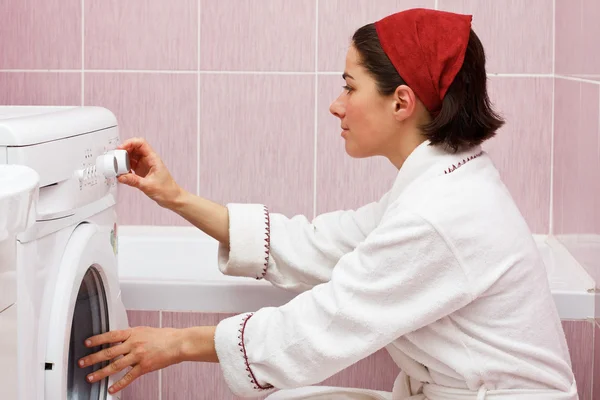 Ung kvinna använder tvättmaskin Stockbild