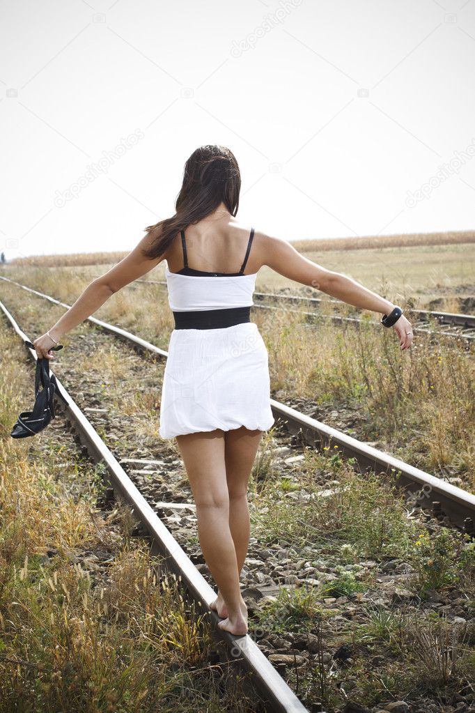 Picture of young woman with sandal in hand on the railway