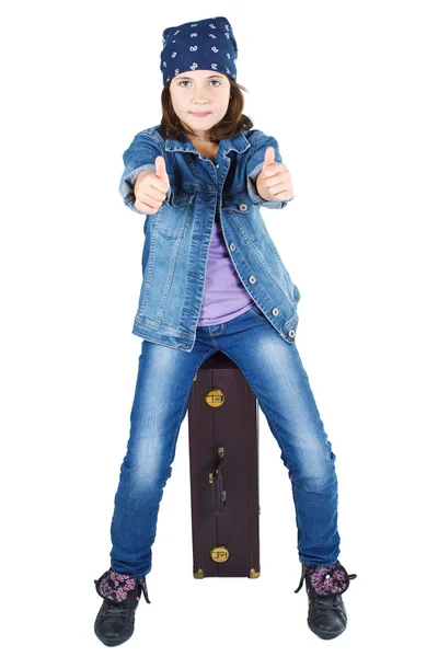 Симпатичная девушка сидит на чемодане с большими пальцами вверх — стоковое фото