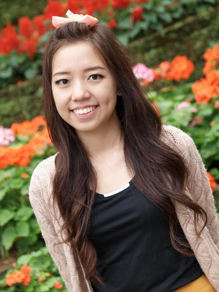 Um sorriso da Ásia menina bonita em um fundo de flor colorida — Fotografia de Stock