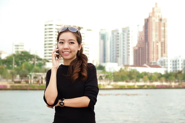 Jonge mooie Aziatische bellen via de telefoon met de bouw van de achtergrond — Stockfoto
