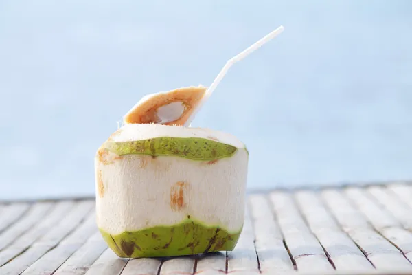 Bebida de água de coco na mesa de bambu com fundo do mar — Fotografia de Stock