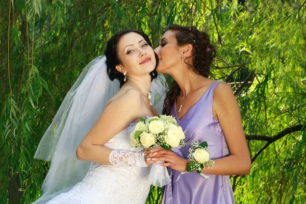 La jovencita besa a la novia sobre un fondo de hojas verdes — Foto de Stock
