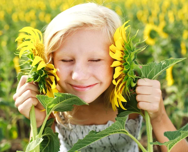 Ung flicka i fältet spelar med solrosor — Stockfoto