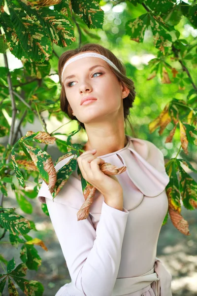 Attractive young blonde girl dreaming in green-brown foliage — Stock Photo, Image