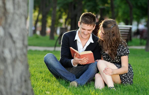 Boy and girl reading a book sitting on the grass — Stock Photo, Image
