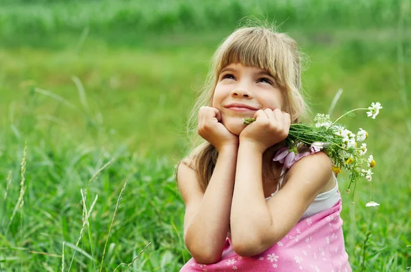 Mladá dívka sedí na pole s kytici — Stock fotografie