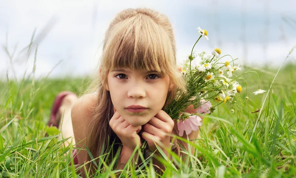 Das junge Mädchen liegt im Gras und hält Blumen — Stockfoto