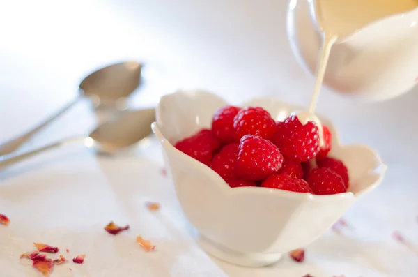 Cream Pouring From a Jug Over Fresh Raspberries Stock Photo