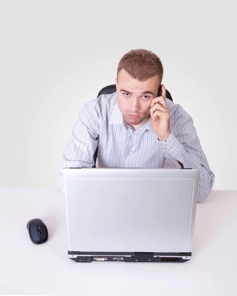 Upptagen ung man med en dator laptop och mobiltelefon i hans kontor — Stockfoto