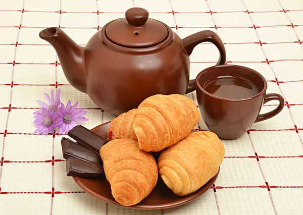 Hnědá čajník, pohár a sauser s croissantem — Stock fotografie