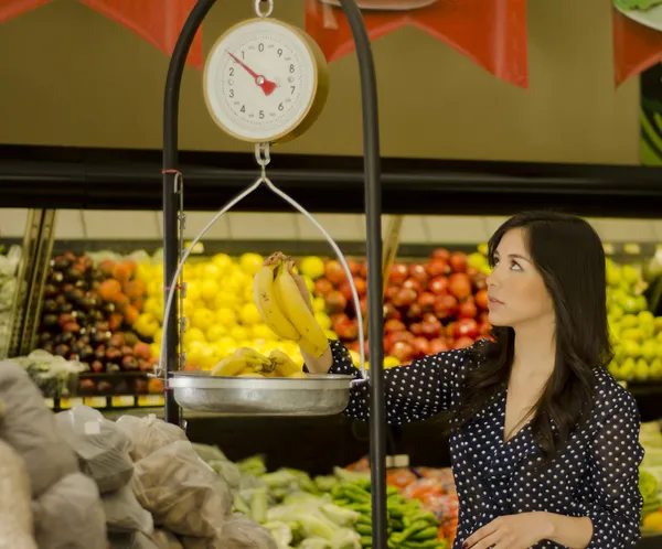 Joven hermosa mujer que pesa frutas en una balanza en un supermercado — Foto de Stock