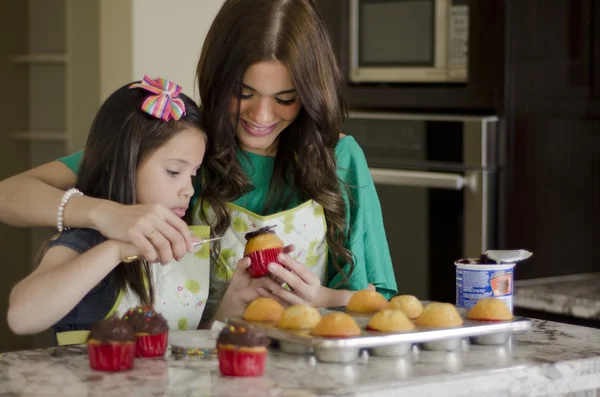 Young beautiful mother decorating cupcakes with daughter — Stock Photo, Image