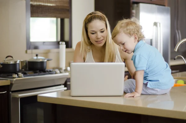 Unga vackra mamma visar något till sin son i sin laptop — Stockfoto