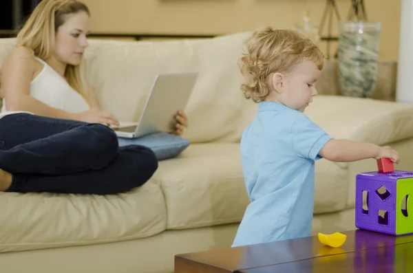 Cute boy playing with a puzzle while mom works — Stock Photo, Image