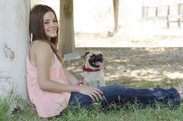 Nette junge Frau sitzt neben einem Baum mit ihrem Mops Hund — Stockfoto