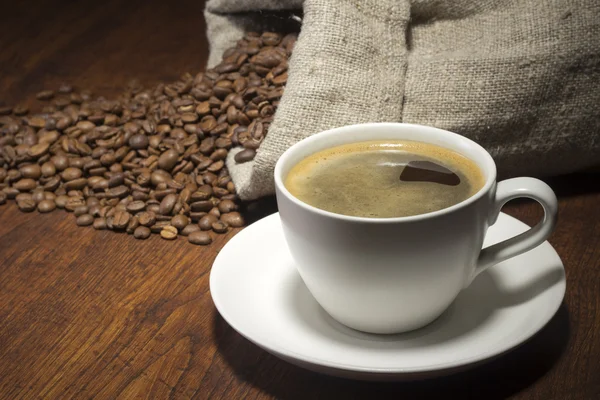 Tazza di caffè e chicchi di caffè da borsa su tavolo di legno — Foto Stock